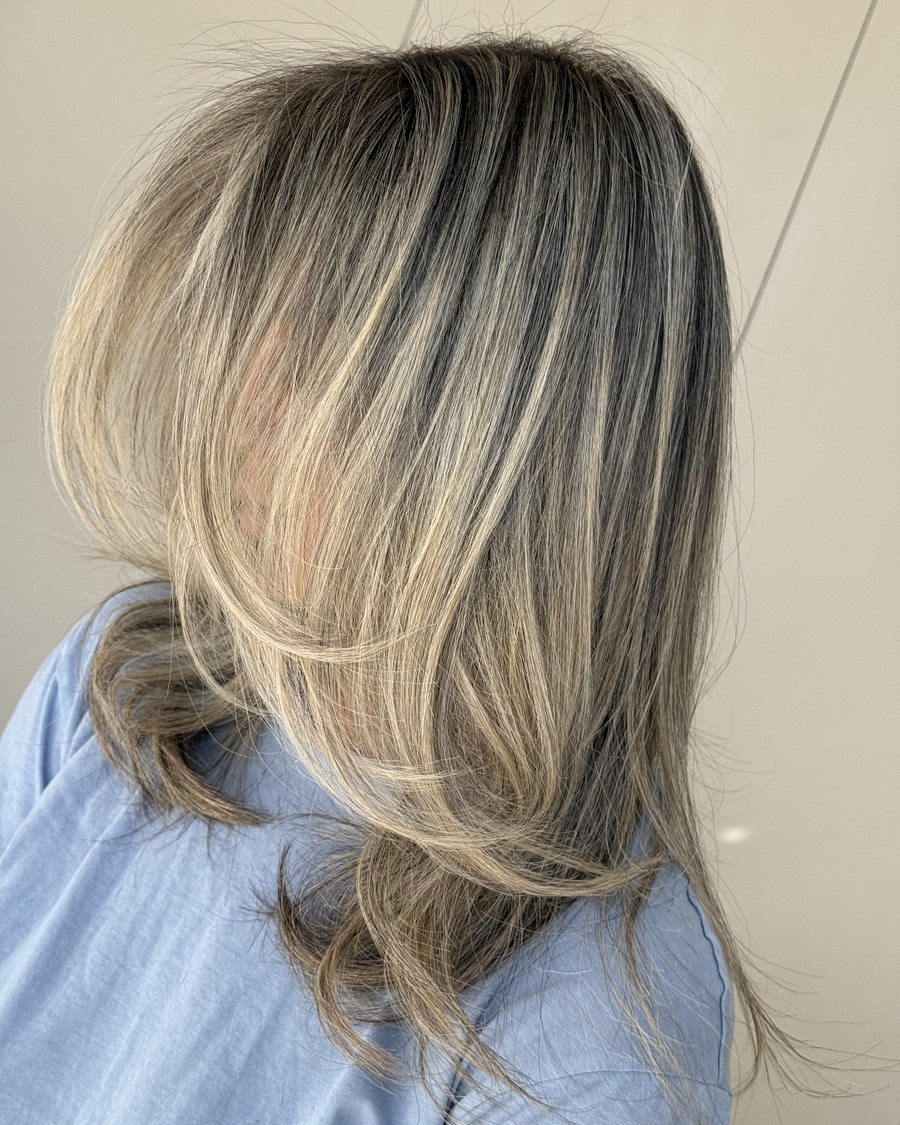 Shoulder-length hair with ash-blonde highlights over a dark base, blow-dried with the ends curled under.