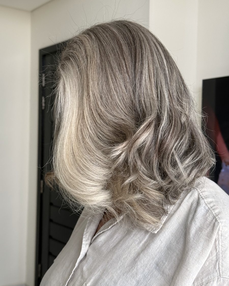 Shoulder-length hair cut to a blunt lob, ash-blonde over a darker root, waved through the ends.